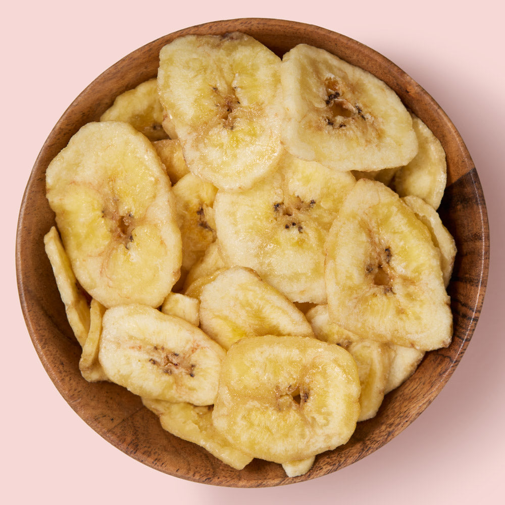 Dried banana chips in a wooden bowl on a pink background healthy snacking UK