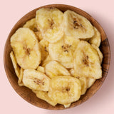 Dried banana chips in a wooden bowl on a pink background healthy snacking UK