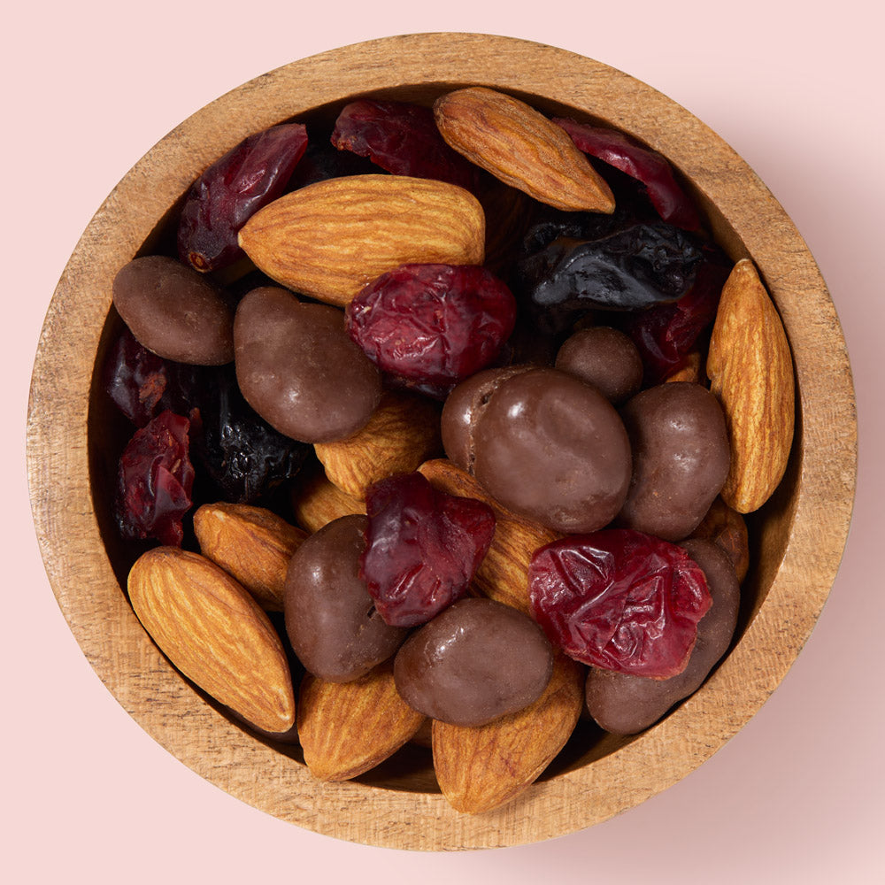 Wooden bowl filled with a mix of almonds, dried cranberries, and chocolate-dipped almonds on a pink background healthy snacking UK