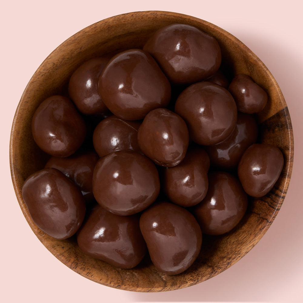 Wooden bowl filled with chocolate-covered raspberries on a pink background healthy snacking UK