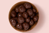 Wooden bowl filled with chocolate-covered raspberries on a pink background
