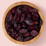 Wooden bowl filled with dried cranberries on a pink background healthy snacking UK