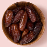 Shot of deglet nour dates in a brown bowl on a pink background healthy snacking UK