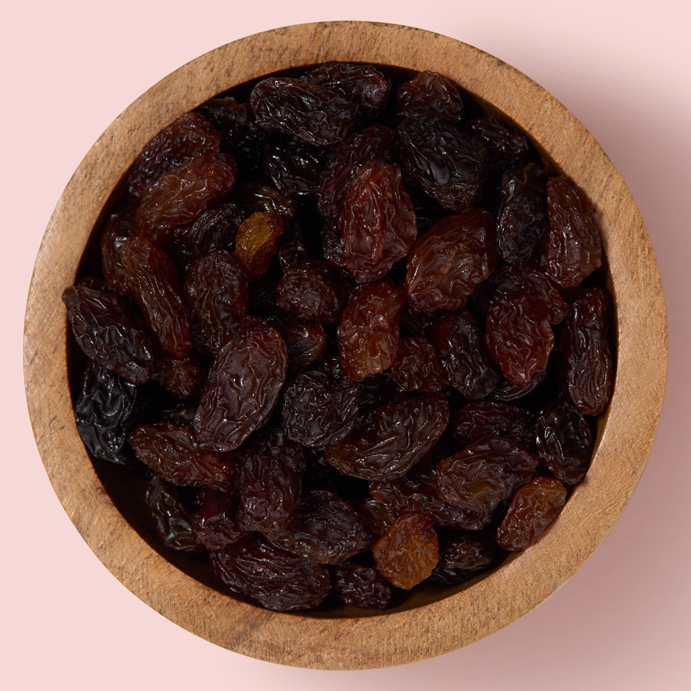 Wooden bowl filled with sultanas on a pink background healthy snacking UK