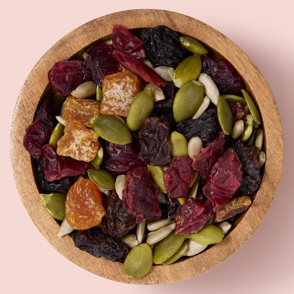 Wooden bowl filled with a mix of dried fruits and seeds on a pink background healthy snacking UK