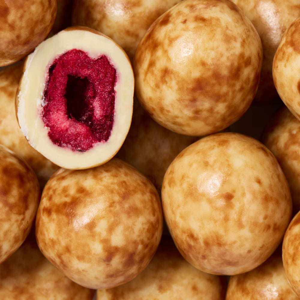 Close-up of round chocolate-covered cherrries, with one cut open to reveal a bright pink-red fruit filling.