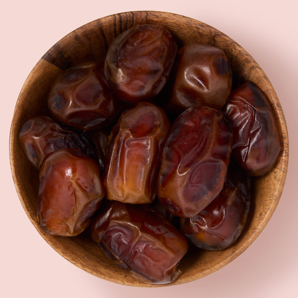 Wooden bowl filled with zamli dates on a light pink background healthy snacking UK