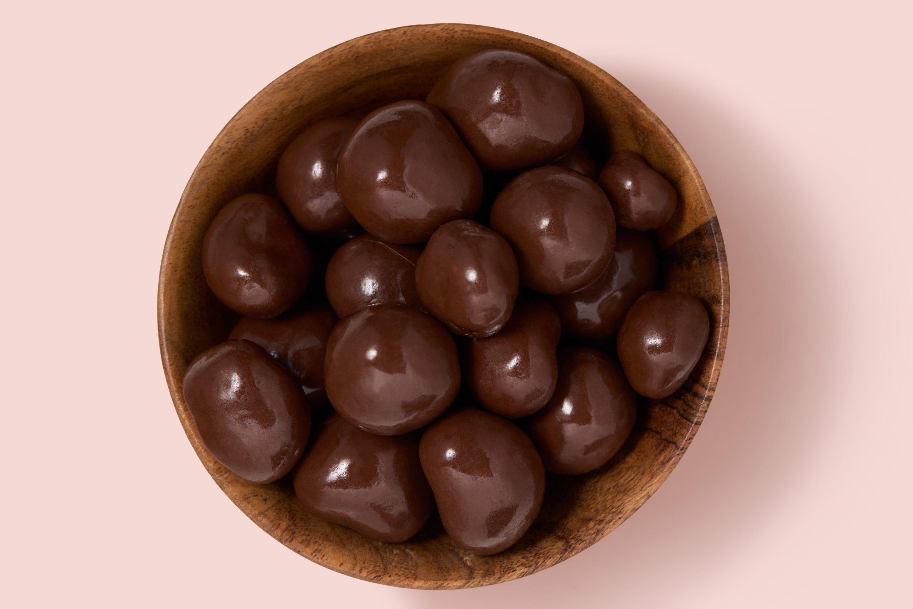 Wooden bowl filled with chocolate-covered raspberries on a pink background