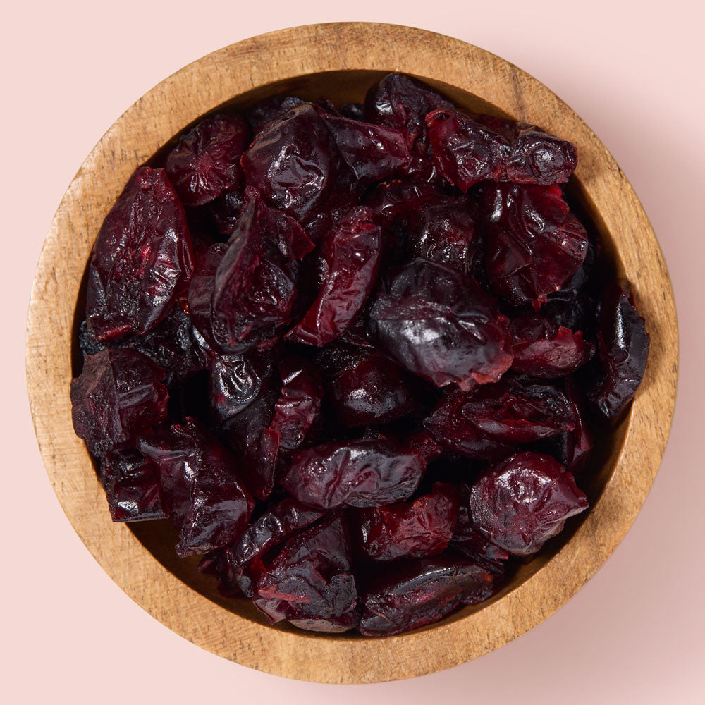 Wooden bowl filled with dried cranberries on a pink background healthy snacking UK