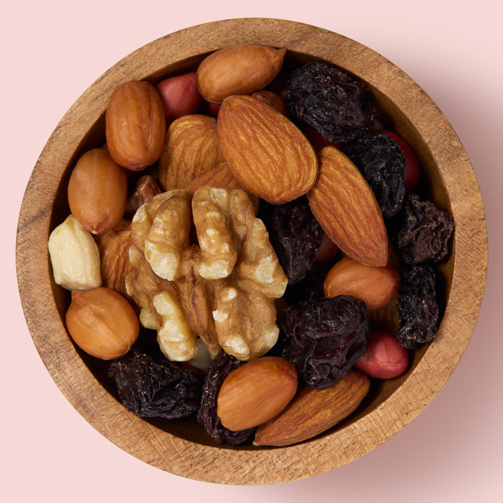 Wooden bowl filled with a mix of nuts and dried fruits on a pink background  healthy snacking UK