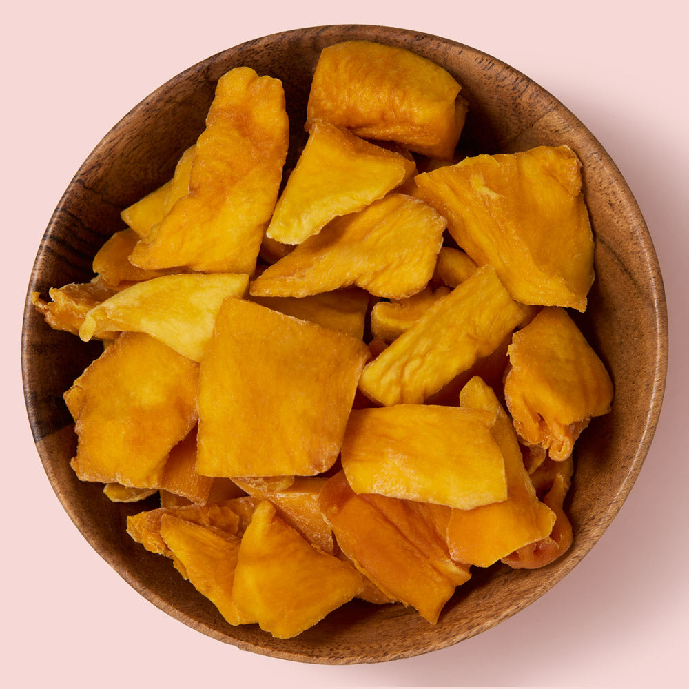 Dried mango chunks in a wooden bowl on a pink background healthy snacking UK
