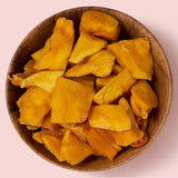 Dried mango chunks in a wooden bowl on a pink background healthy snacking UK