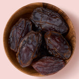 Wooden bowl filled with dark brown medjool dates on a pink background, healthy snacking UK