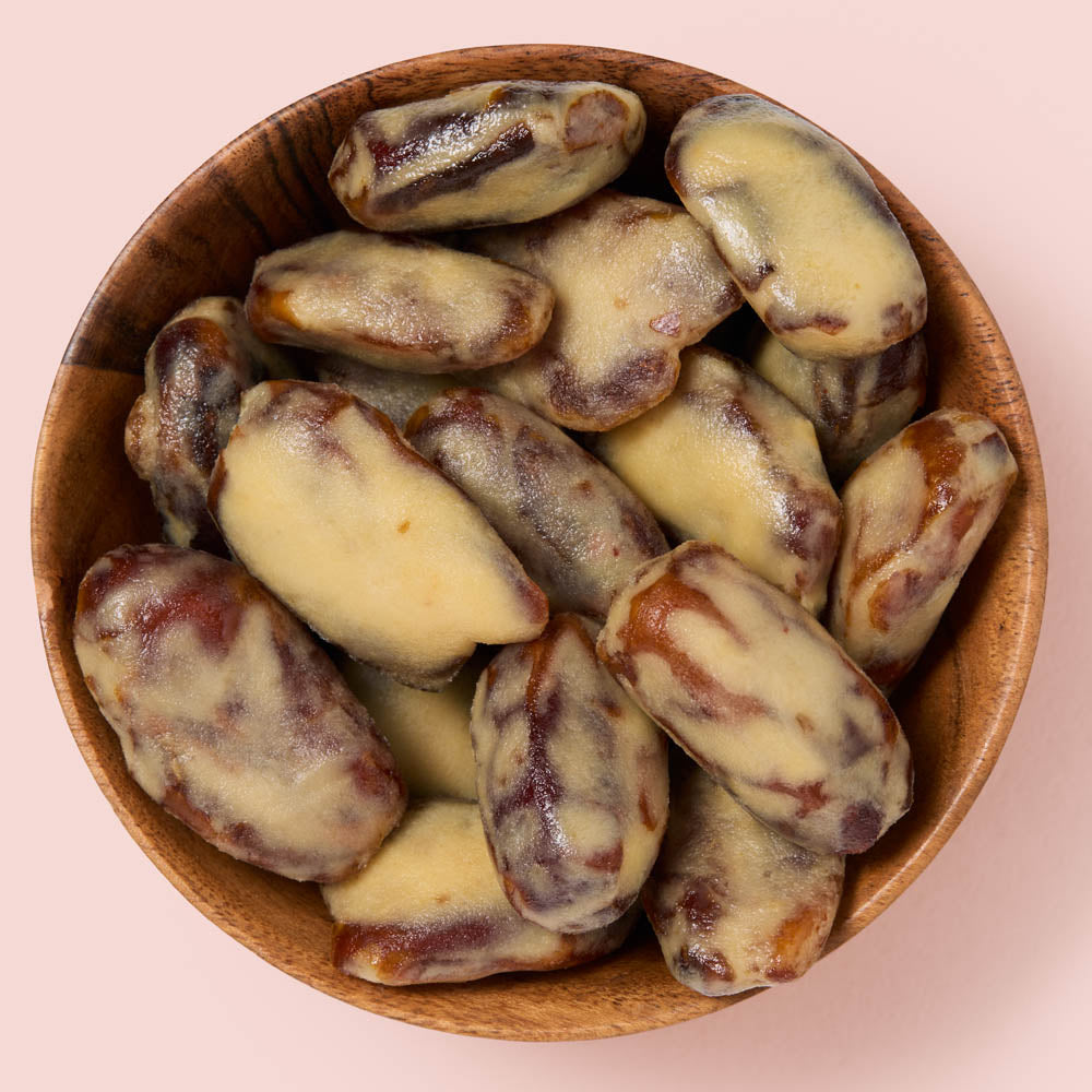 A top-down view of peanut butter dates in a wooden bowl against a solid pale pink background.