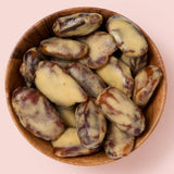 A top-down view of peanut butter dates in a wooden bowl against a solid pale pink background.