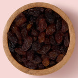 Wooden bowl filled with sultanas on a pink background healthy snacking UK