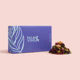 Blue box with 'Palm & Vine' branding next to a pile of dried fruits and seeds  on a pink background. Trail Mixes & Snack Blends – Fuel Your Day, Naturally