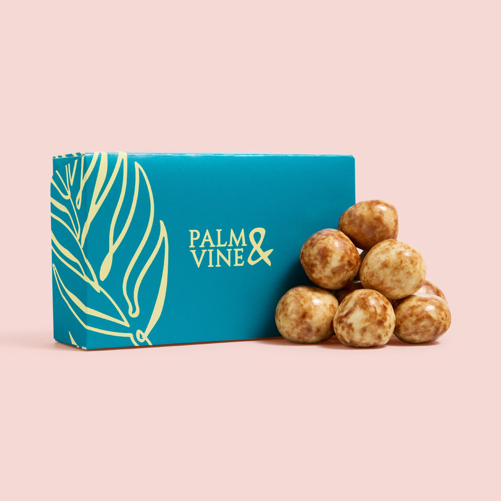 A teal and gold box of Palm & Vine chocolates with a small pyramid of decorated chocolate truffles on a solid pale pink background, healthy snacking UK